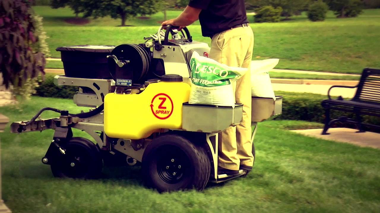 person driving a lawn fertilizing machine across a green lawn